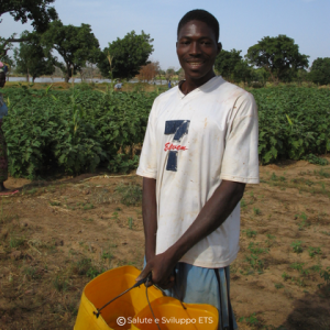 Un giovane ragazzo sorridente lavora in un campo agricolo sostenuto dal 5x1000 di Salute e Sviluppo ETS